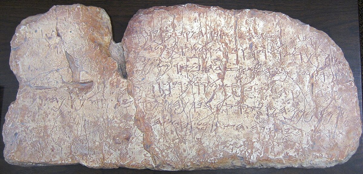 Kopie Šíloašského nápisu z vodního tunelu v Jeruzalémě (kolem 700 př. n. l.): šest řádků paleohebrejského písma, slova oddělují tečky. Originál je v Archeologických muzeích v Istanbulu.