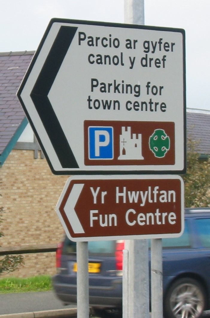 Dvojjazyčný směrový ukazatel v Caernarfonu na severozápadě Walesu: velšský text stojí nad anglickým (Parcio ar gyfer canol y dref – Parking for town centre).